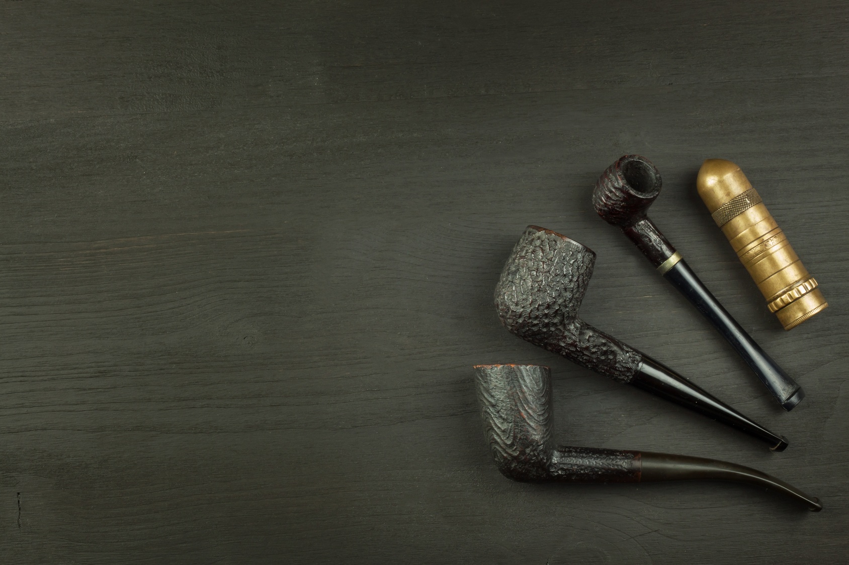 Old tobacco pipe used on a black wooden background. Shabby old tobacco pipe. Wooden tobacco pipe on a black background.